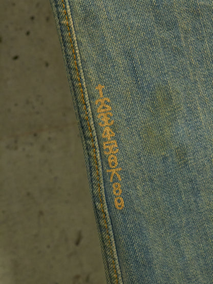 Close-up of blue denim fabric with yellow stitching on a textured gray background
