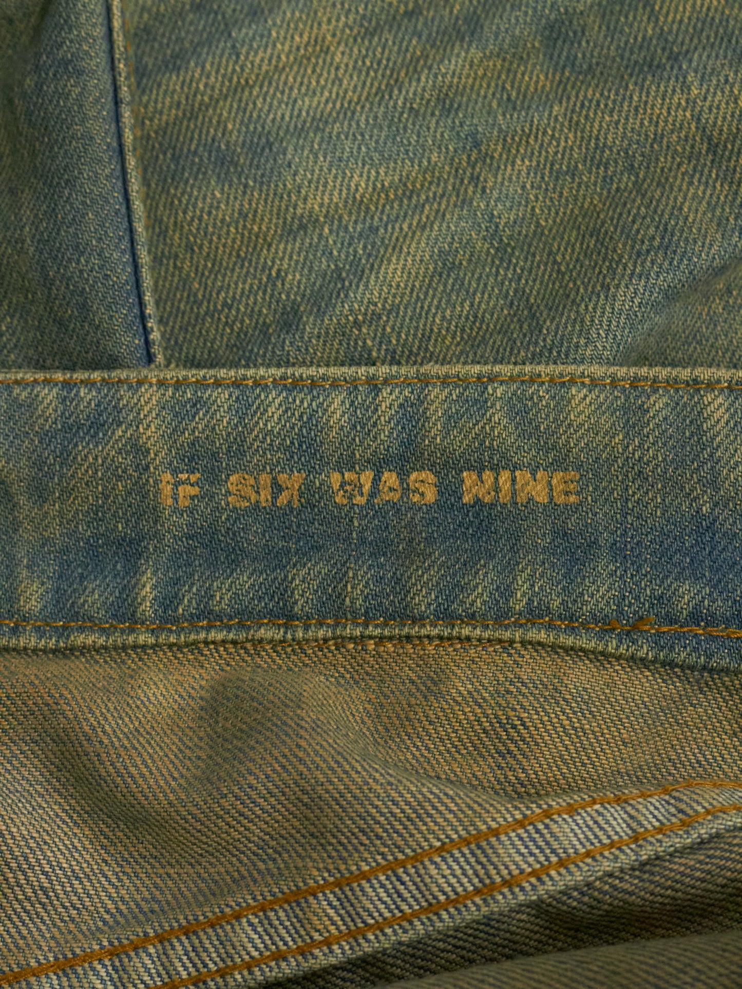 Close-up of denim fabric with 'If Six Was Nine' embroidery.