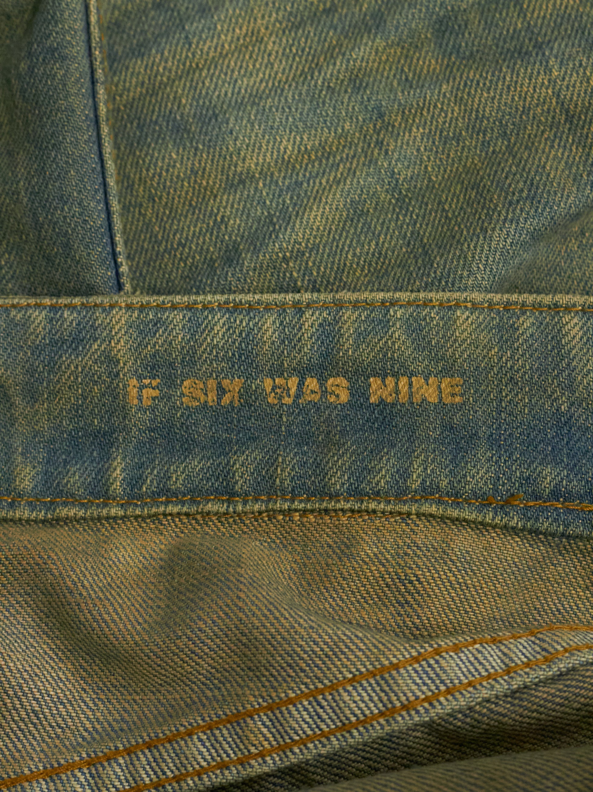 Close-up of denim fabric with 'If Six Was Nine' embroidery.