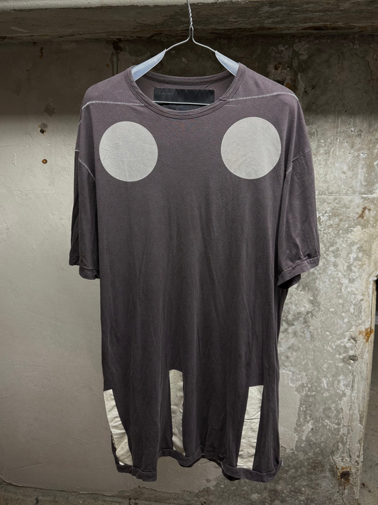 Brown t-shirt with white circular designs on a hanger against a textured wall.