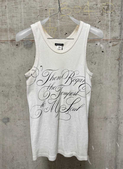 An off-white tank top with black cursive text reading 'Then began the Tempest to My Soul' hanging on a clear plastic hanger against a textured concrete wall.