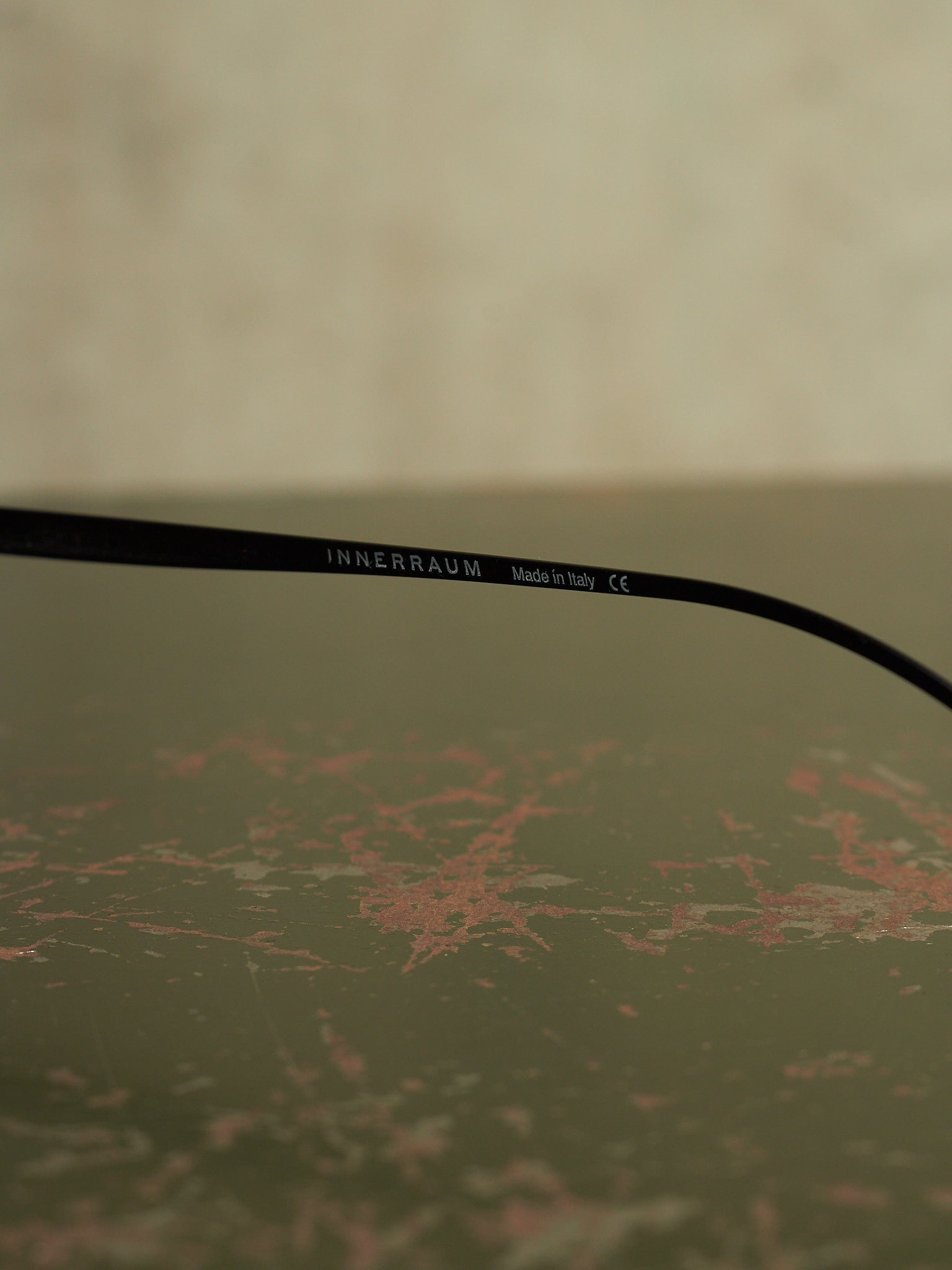 A close-up of a black optical temple arm with the brand name 'INNERRAUM' printed in white, resting on a textured, distressed olive-green surface.