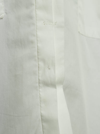 Close-up detail of a white fabric garment showing a vertical seam, button placket stitching, and a pocket edge.