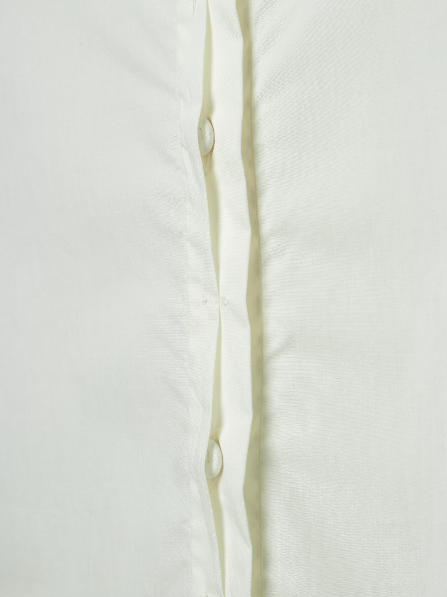 Close-up of a white button-up shirt showing the front placket with white buttons and a subtle vertical crease.