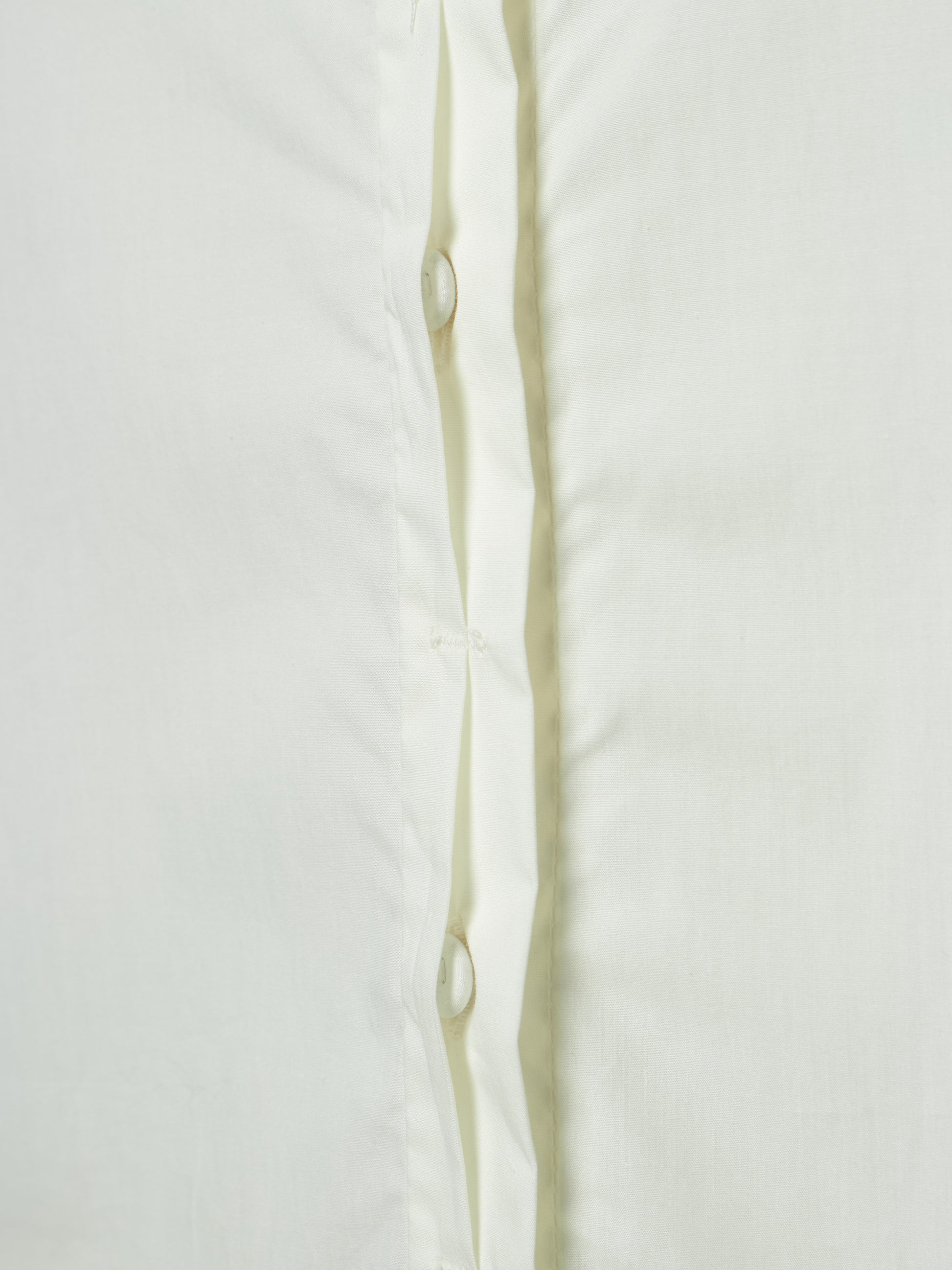 Close-up of a white button-up shirt showing the front placket with white buttons and a subtle vertical crease.