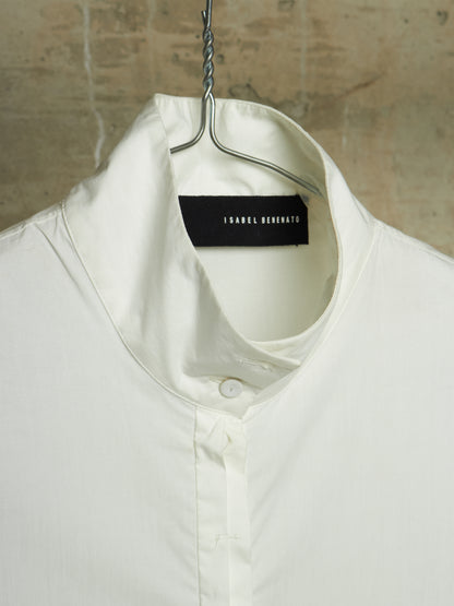 A close-up of a white collared shirt hanging on a metal hanger against a textured beige wall. The brand label 'ISABEL MARANT' is visible inside the collar.