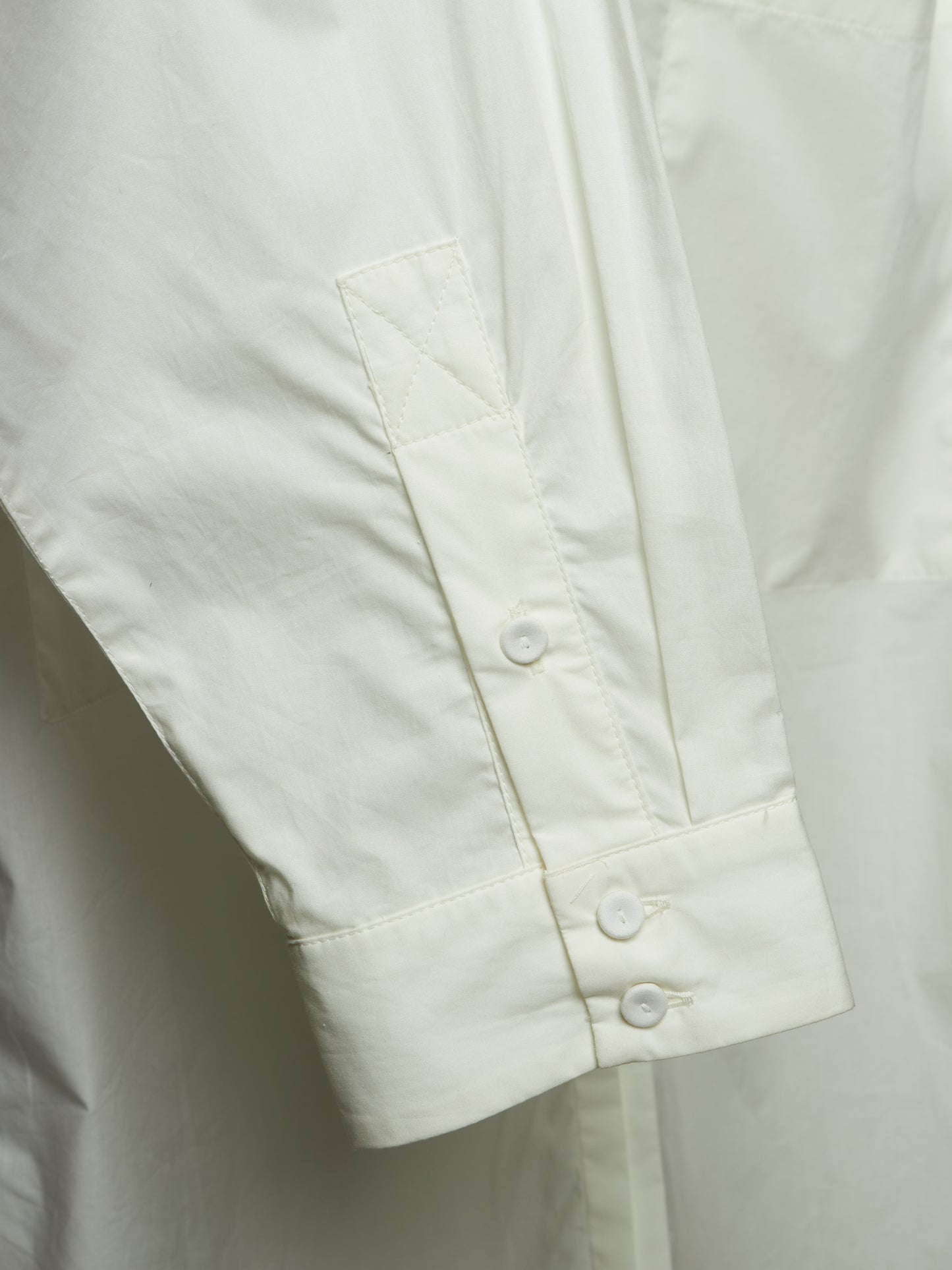 Close-up of a white long-sleeve shirt showing the sleeve cuff with two buttons and a vertical chest pocket.