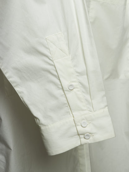 Close-up of a white long-sleeve shirt showing the sleeve cuff with two buttons and a vertical chest pocket.