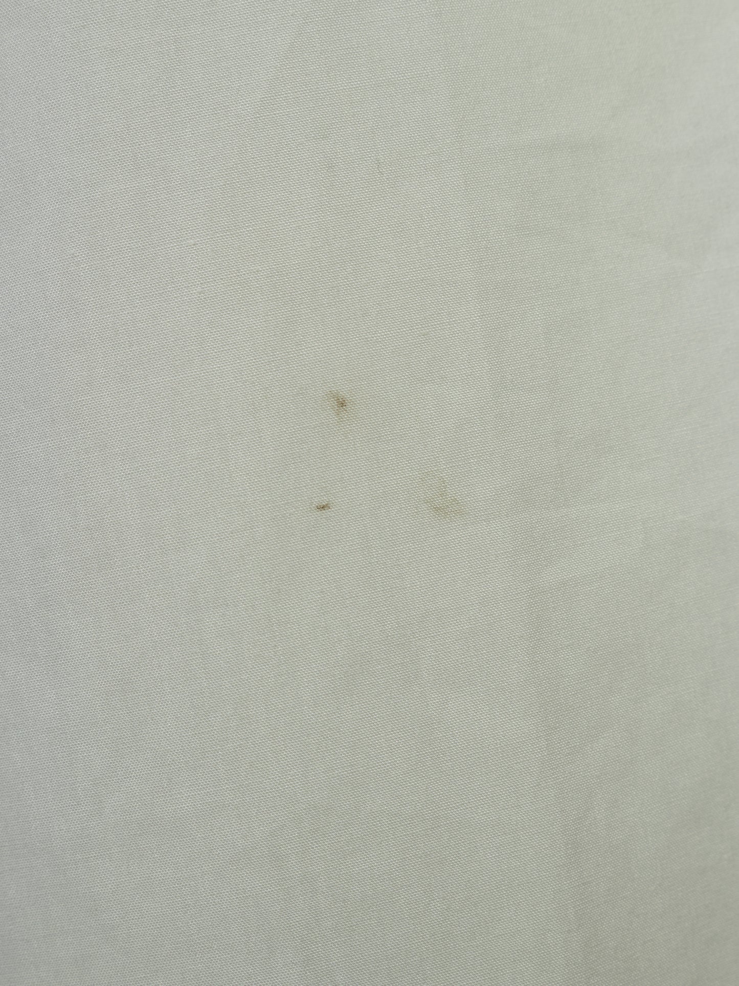 A close-up of a light off-white or cream textured fabric surface with a few small brown specks visible.