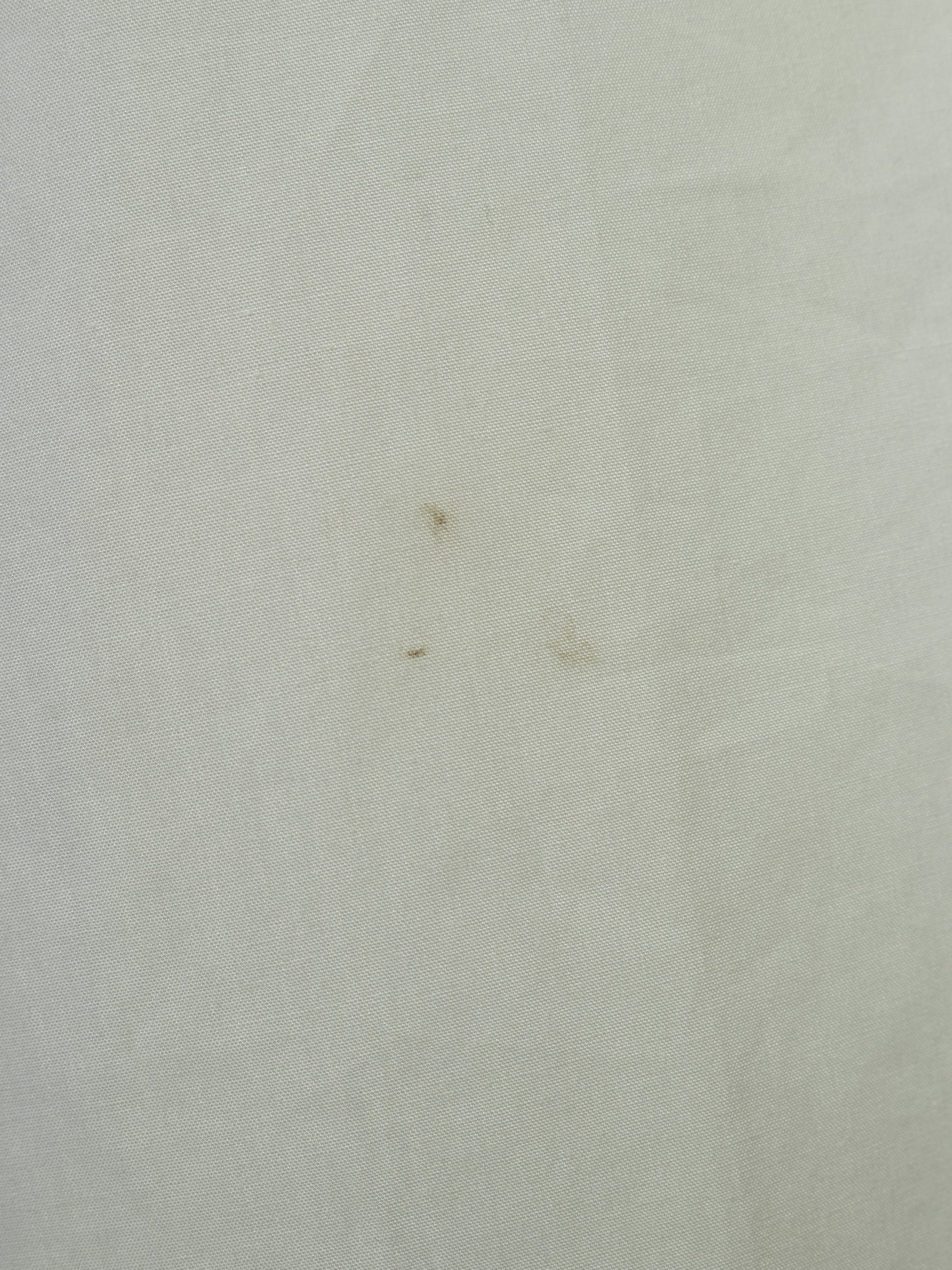 A close-up of a light off-white or cream textured fabric surface with a few small brown specks visible.
