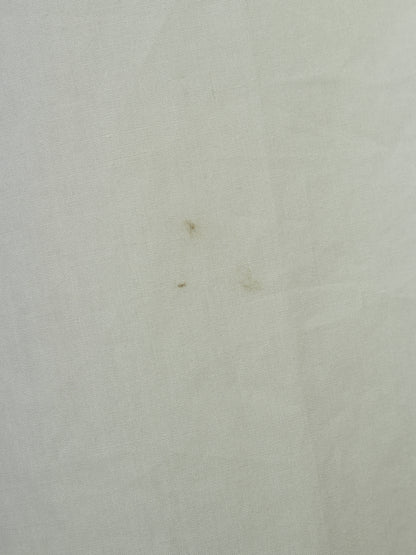A close-up of a light off-white or cream textured fabric surface with a few small brown specks visible.