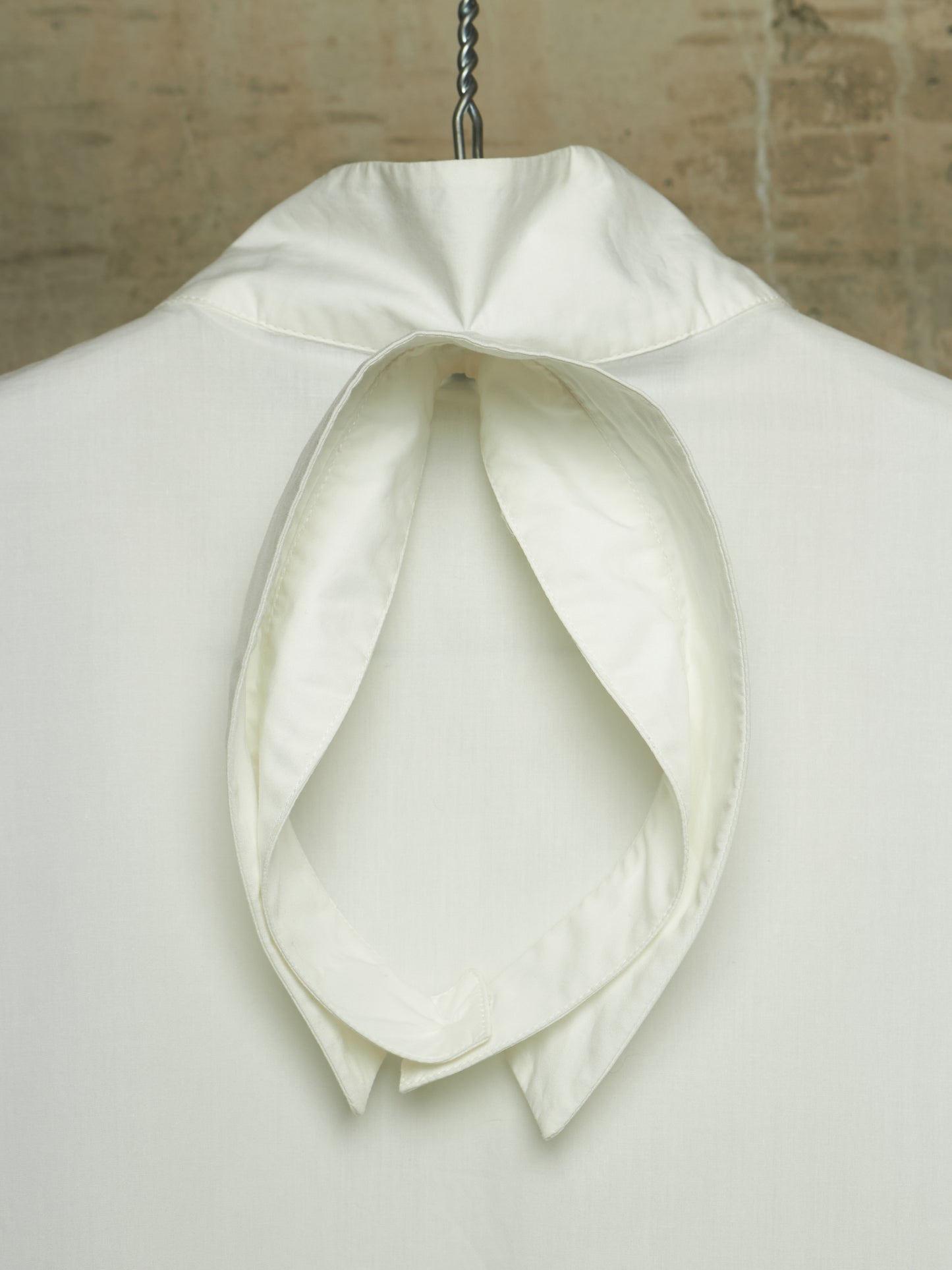 An off-white or cream high-neck cravat collar with a large bow, displayed on a white mannequin torso against a textured beige background.
