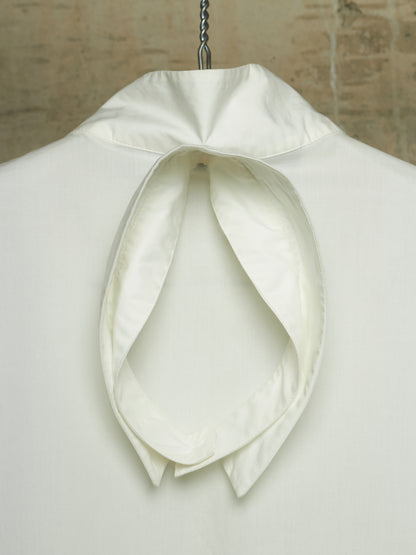 An off-white or cream high-neck cravat collar with a large bow, displayed on a white mannequin torso against a textured beige background.