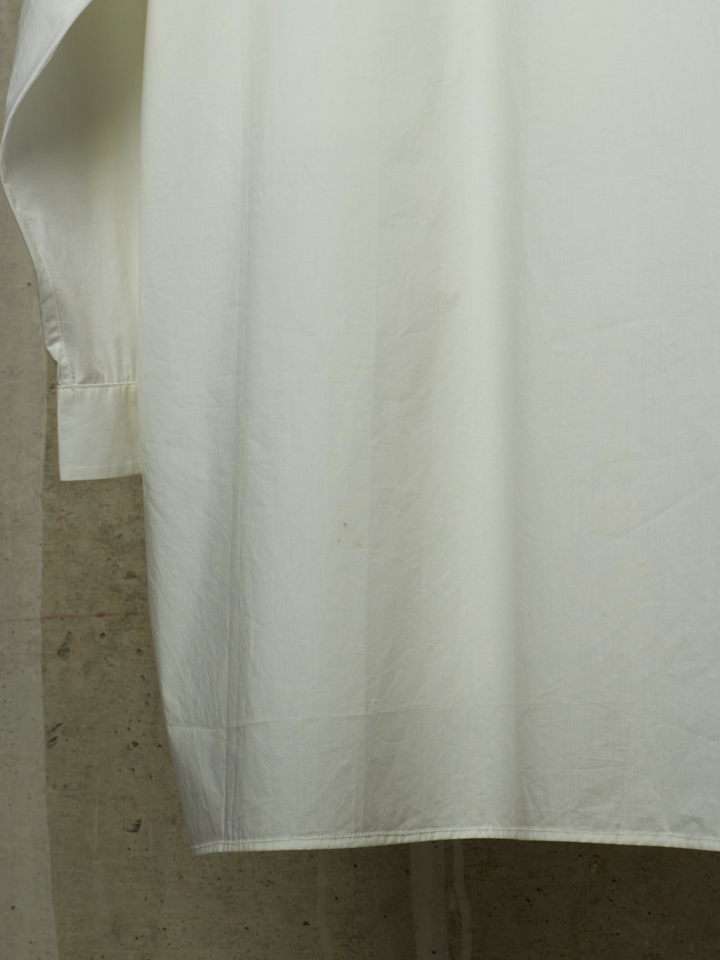 A close-up of a white fabric garment, likely a shirt or dress, showing a cuff and drape against a textured gray background.