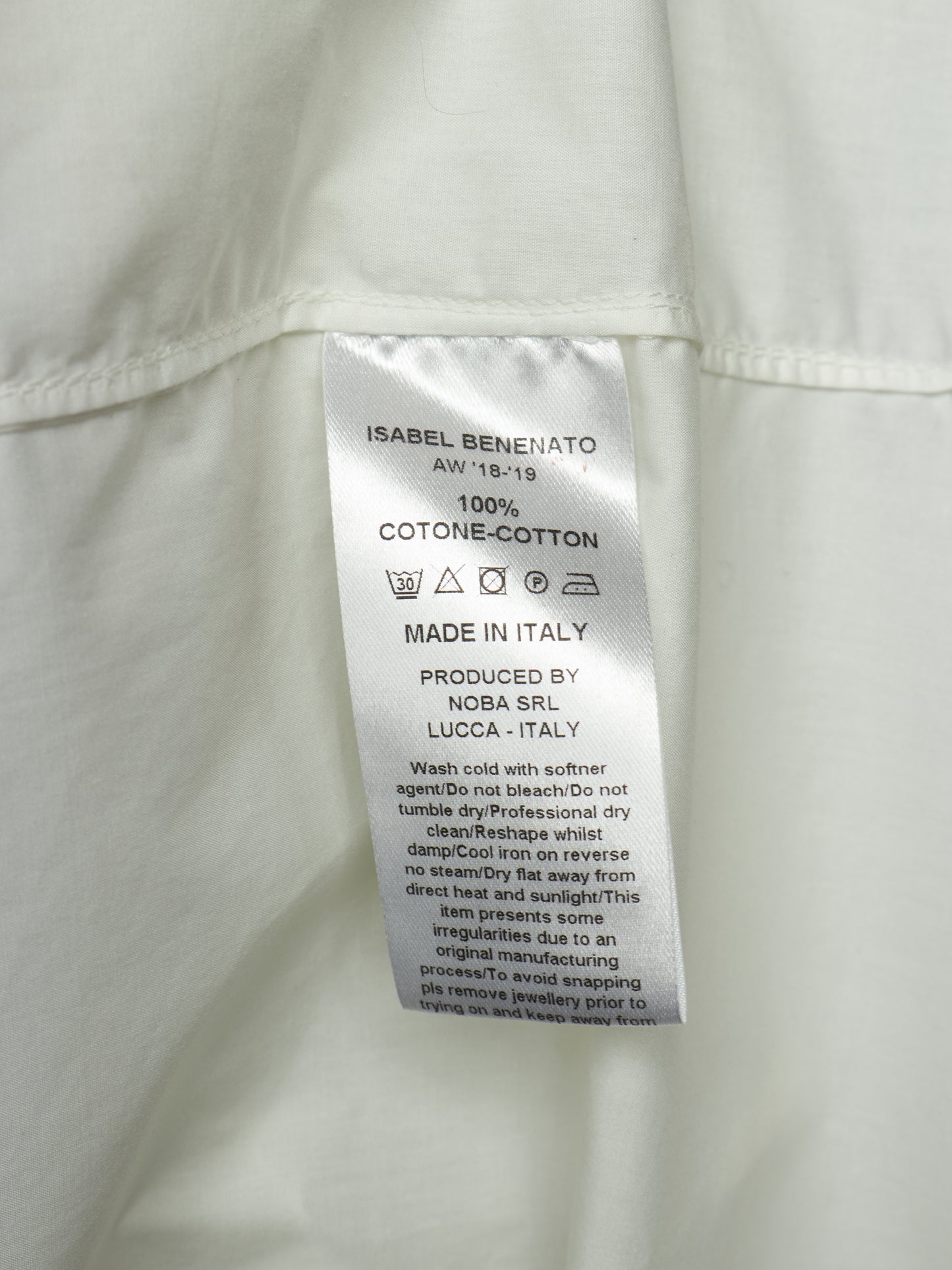 Close-up of a white garment's interior label reading Isabel Benenato, 100% cotton, made in Italy, with care instructions and production details.