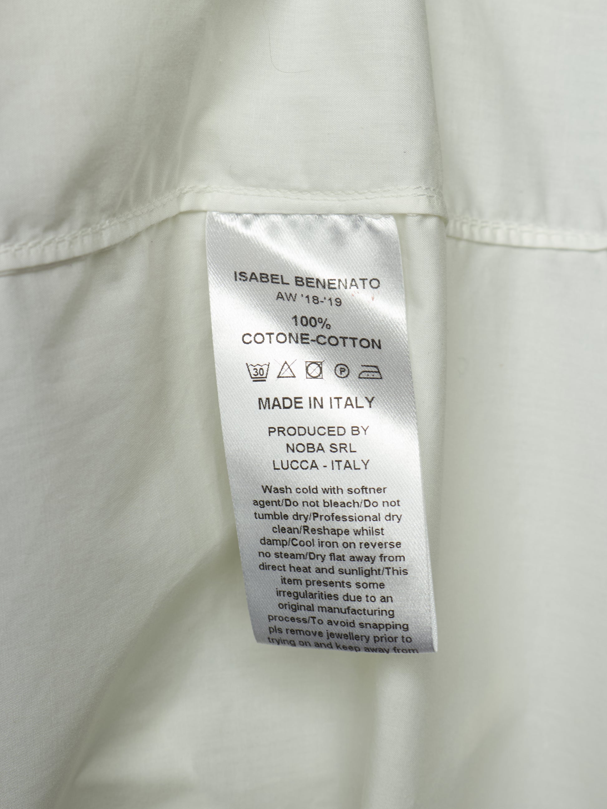 Close-up of a white garment's interior label reading Isabel Benenato, 100% cotton, made in Italy, with care instructions and production details.