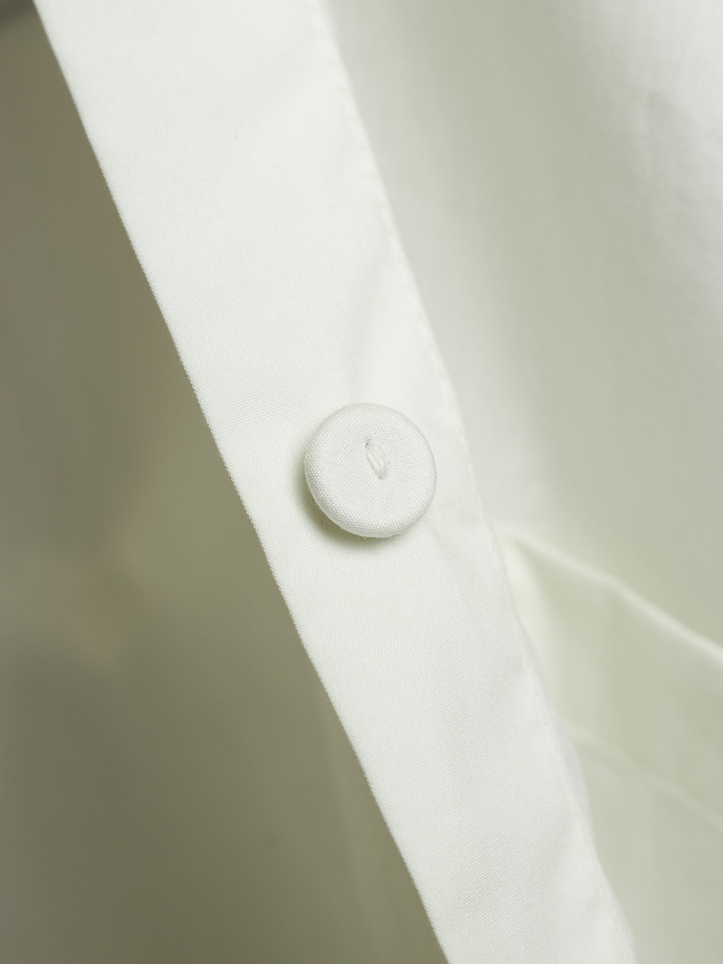 Close-up of a white buttoned collar on a white shirt, showing the fabric texture and a small debossed letter.