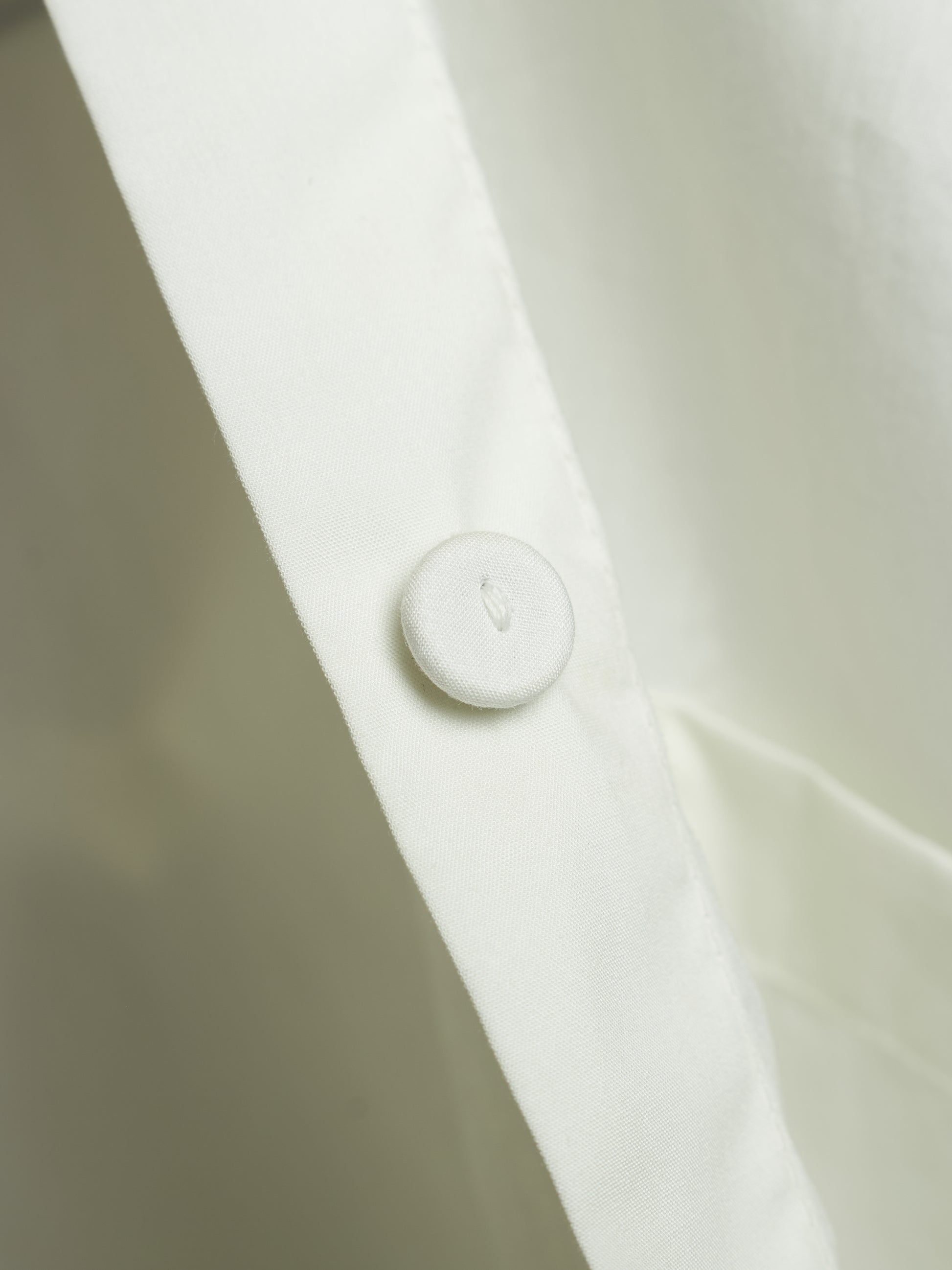 Close-up of a white buttoned collar on a white shirt, showing the fabric texture and a small debossed letter.