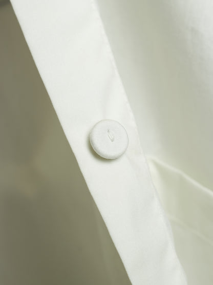Close-up of a white buttoned collar on a white shirt, showing the fabric texture and a small debossed letter.
