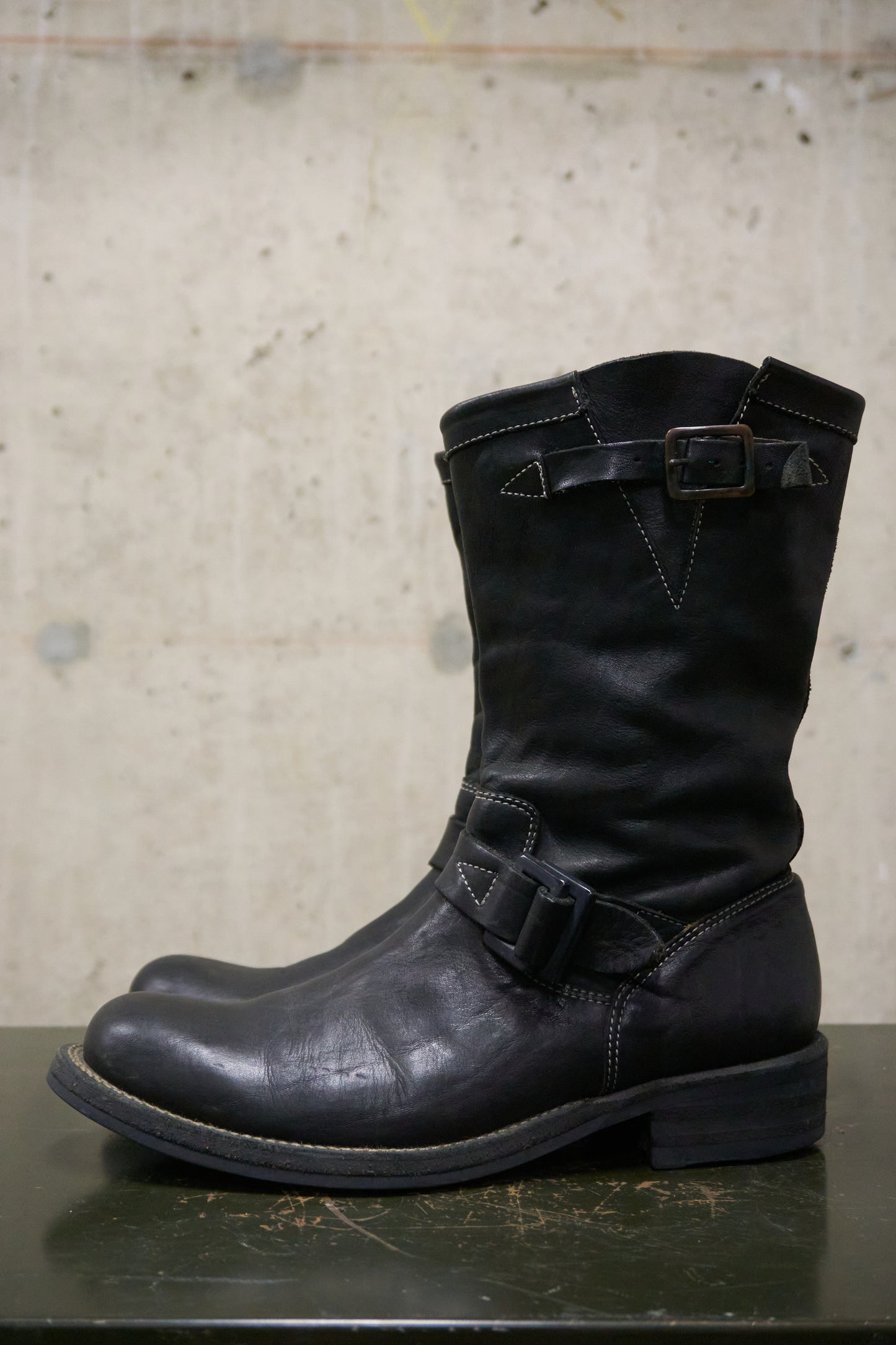 Black leather boot with buckles on a concrete surface