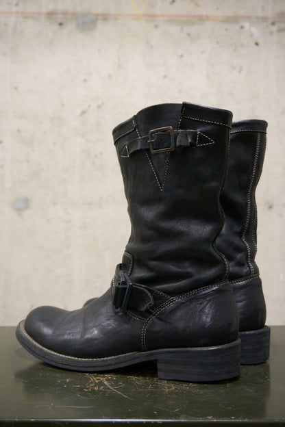 Pair of black leather boots with buckles on a concrete surface