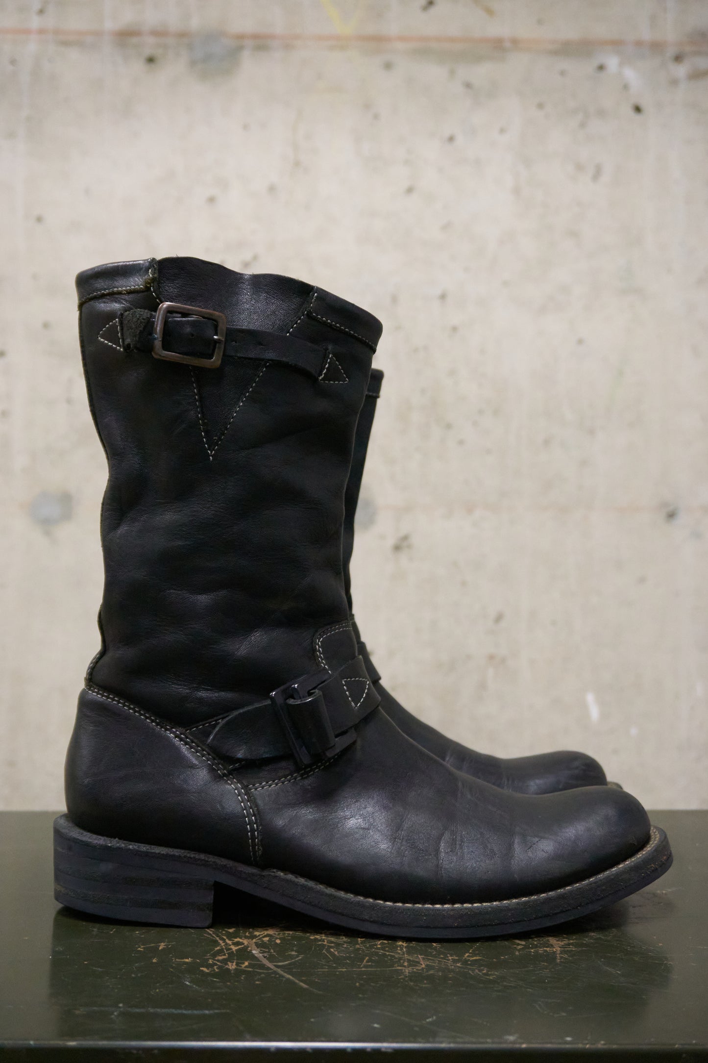 Pair of black leather boots with buckles on a concrete surface