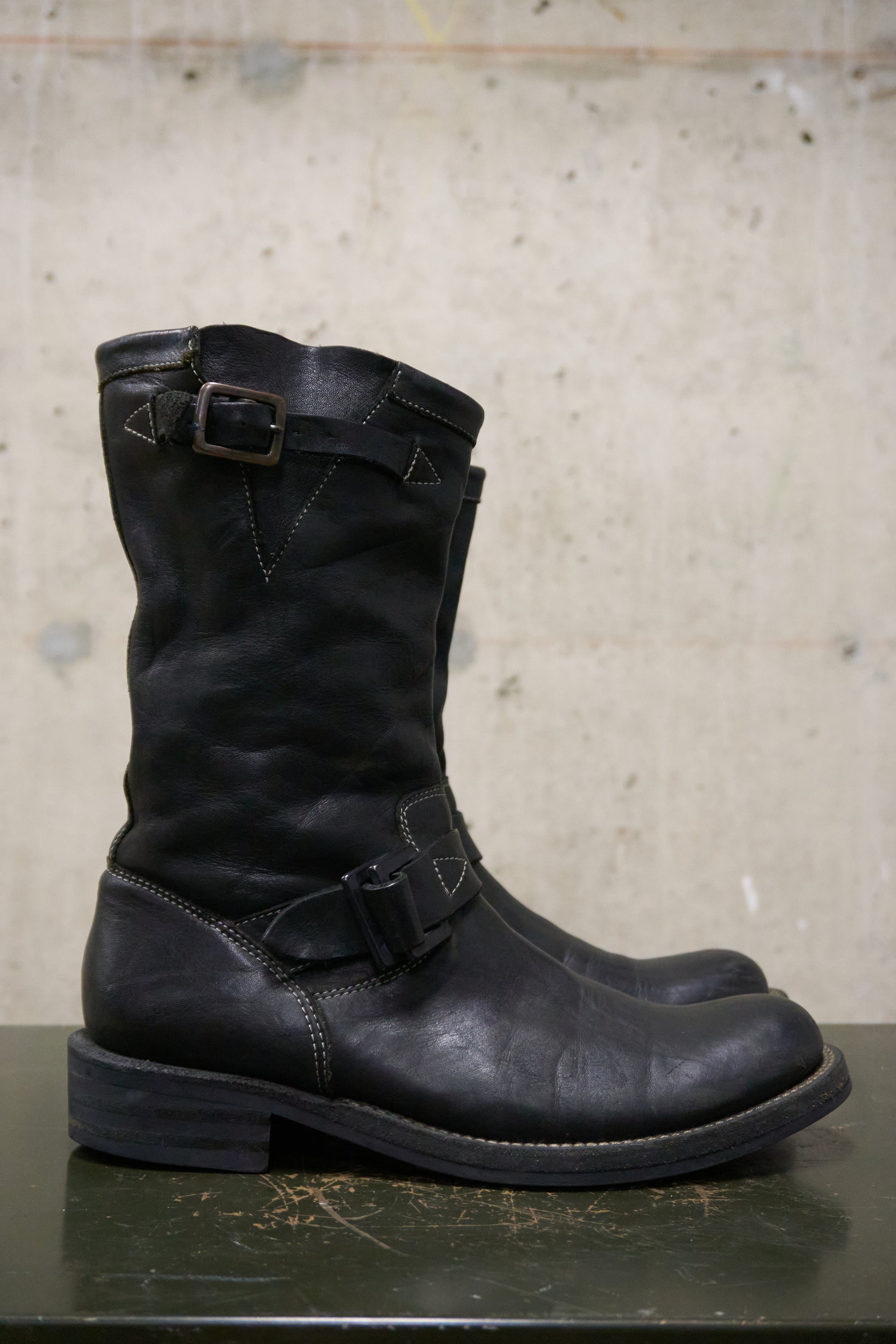 Pair of black leather boots with buckles on a concrete surface