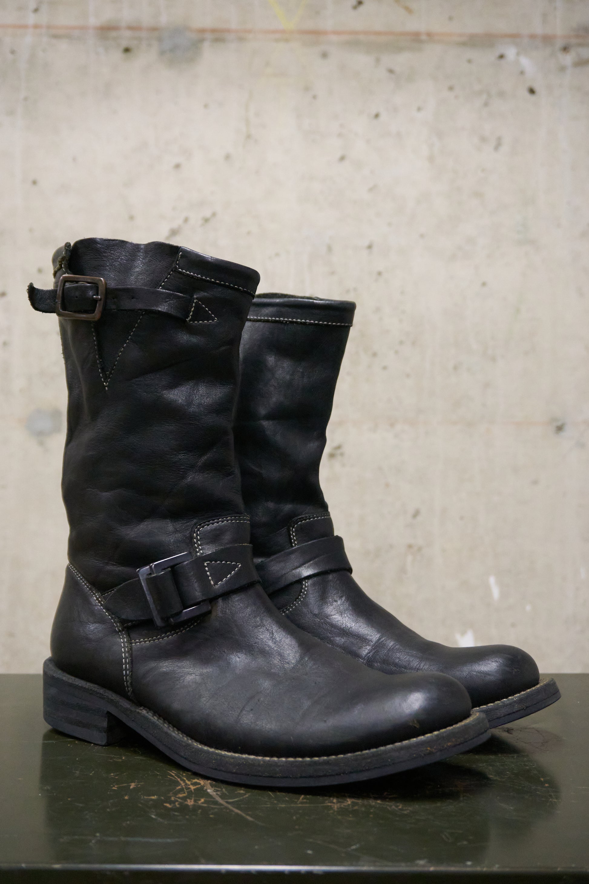 Pair of black leather boots with buckles on a concrete surface