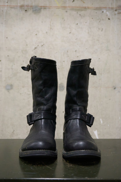 Pair of black leather boots with buckles on a concrete surface