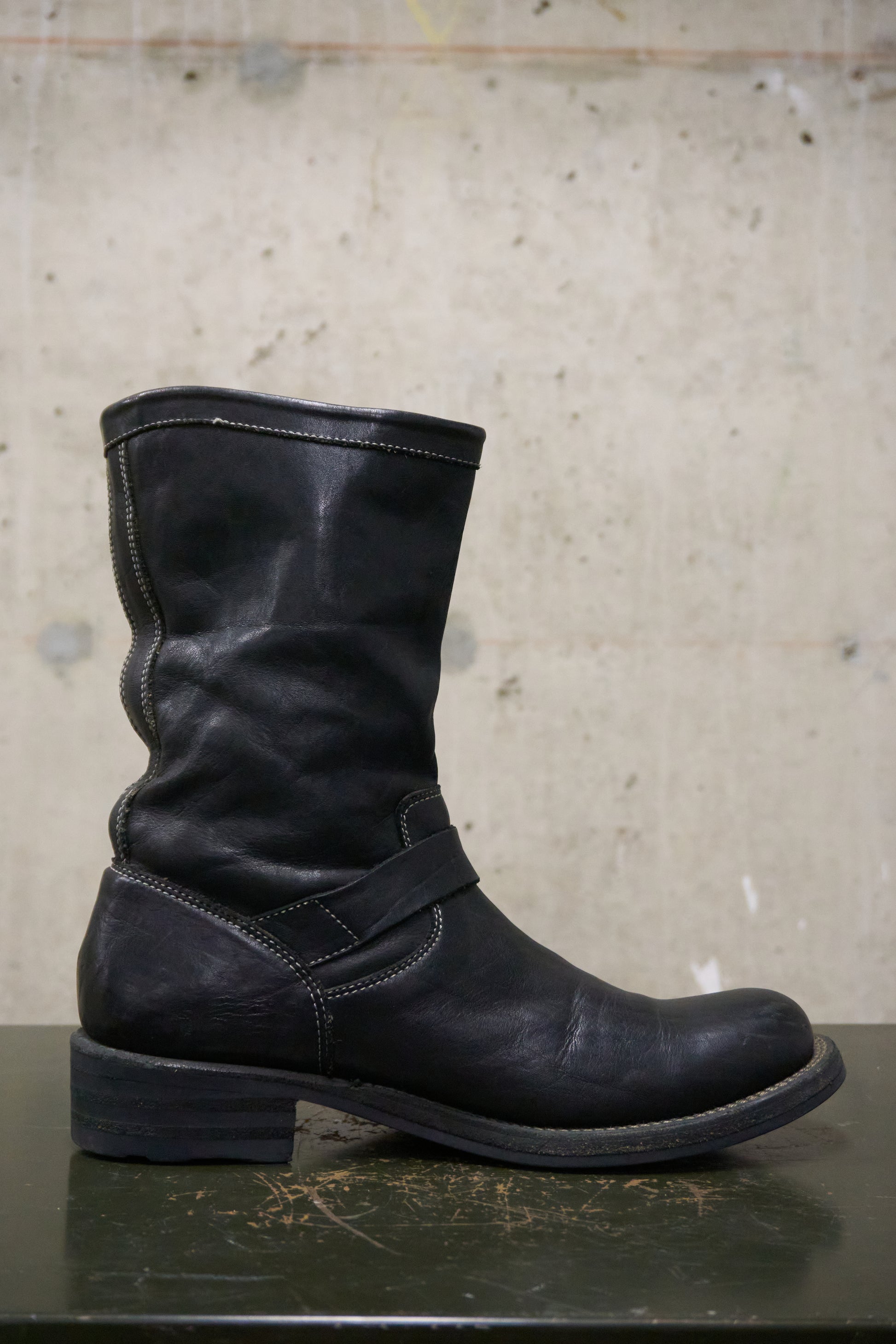 Black leather boot on a reflective surface with a concrete wall background