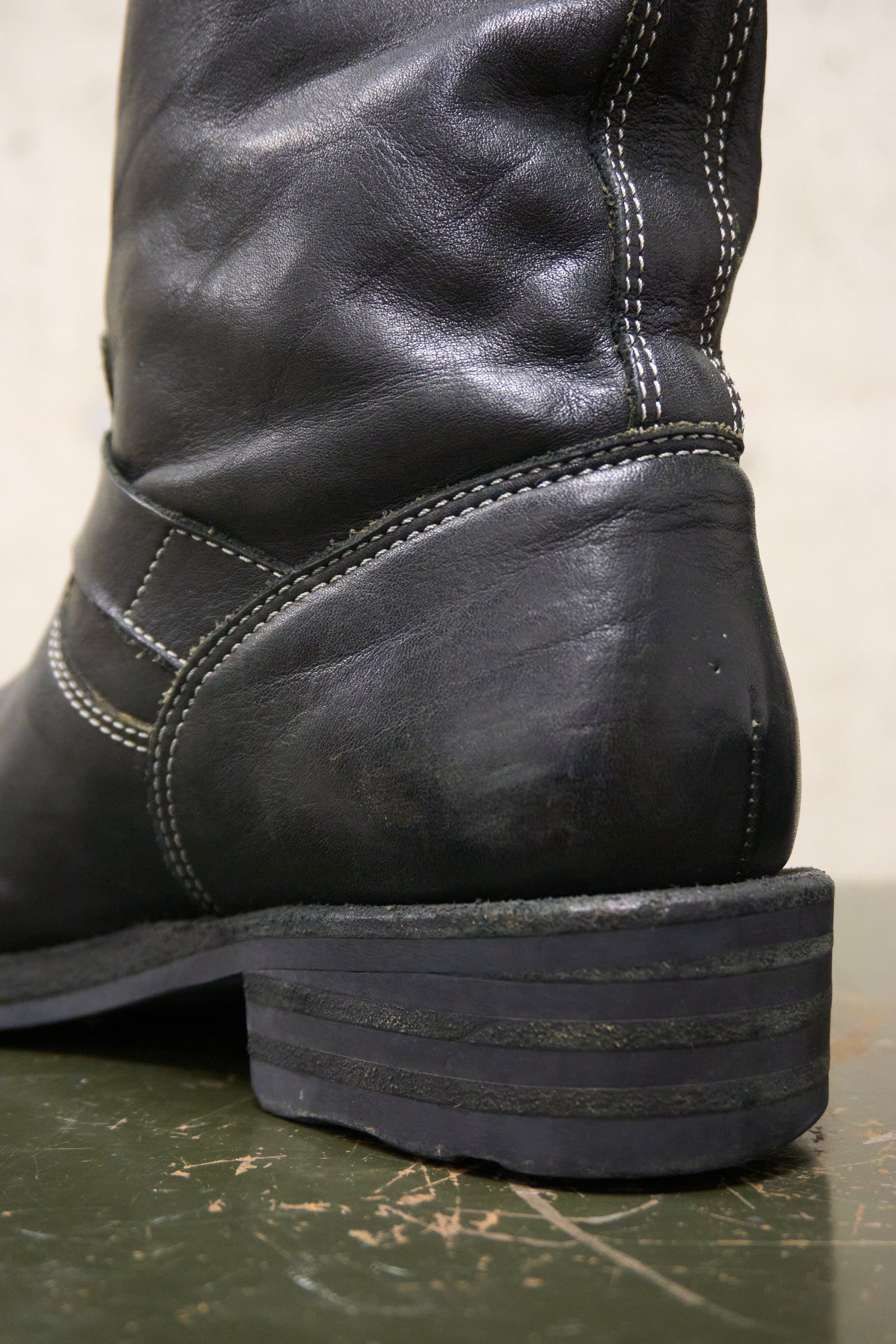 Close-up of a black leather boot with visible stitching on a green surface.