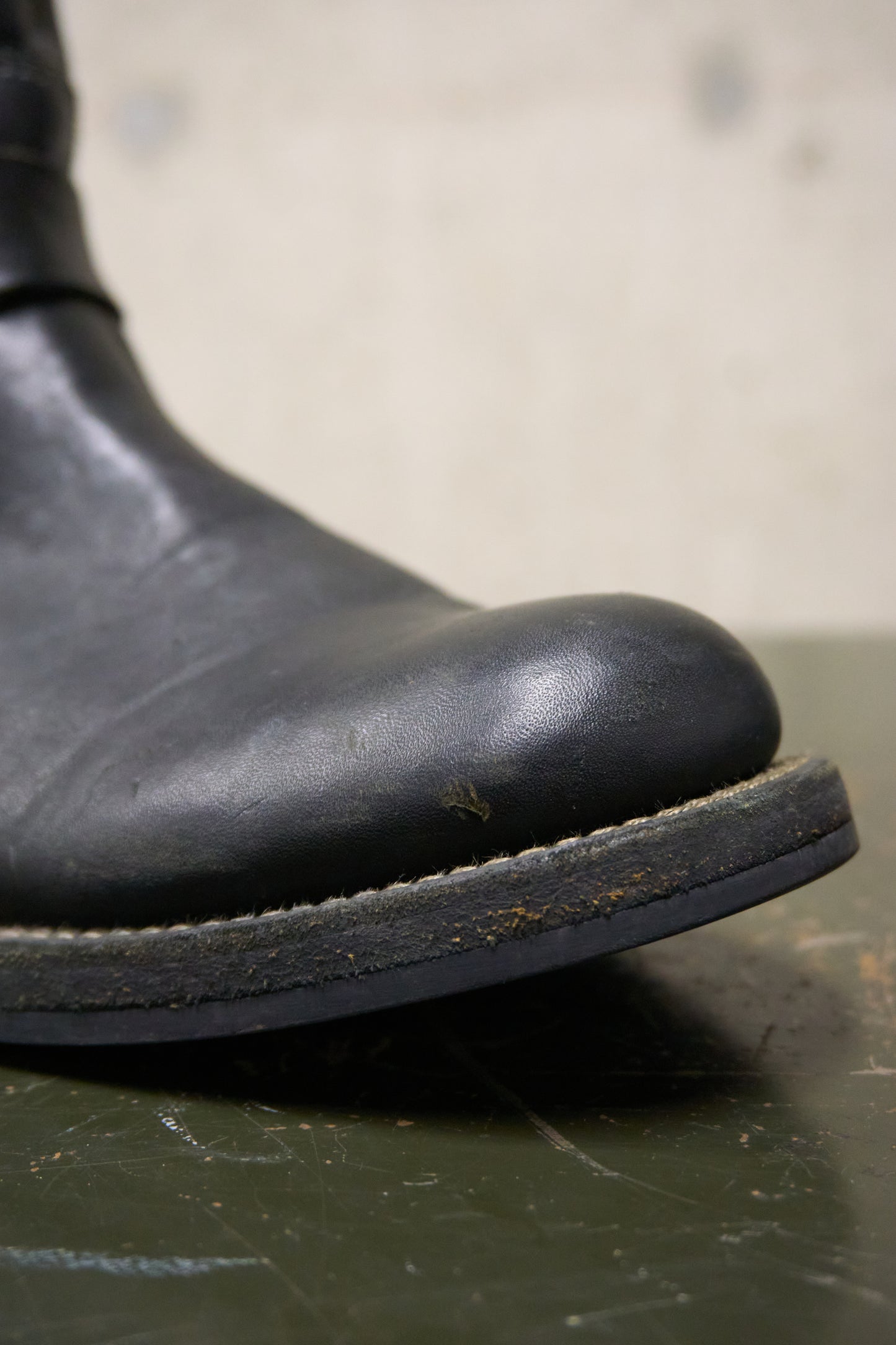 Close-up of a black leather boot sole on a textured surface with a blurred background