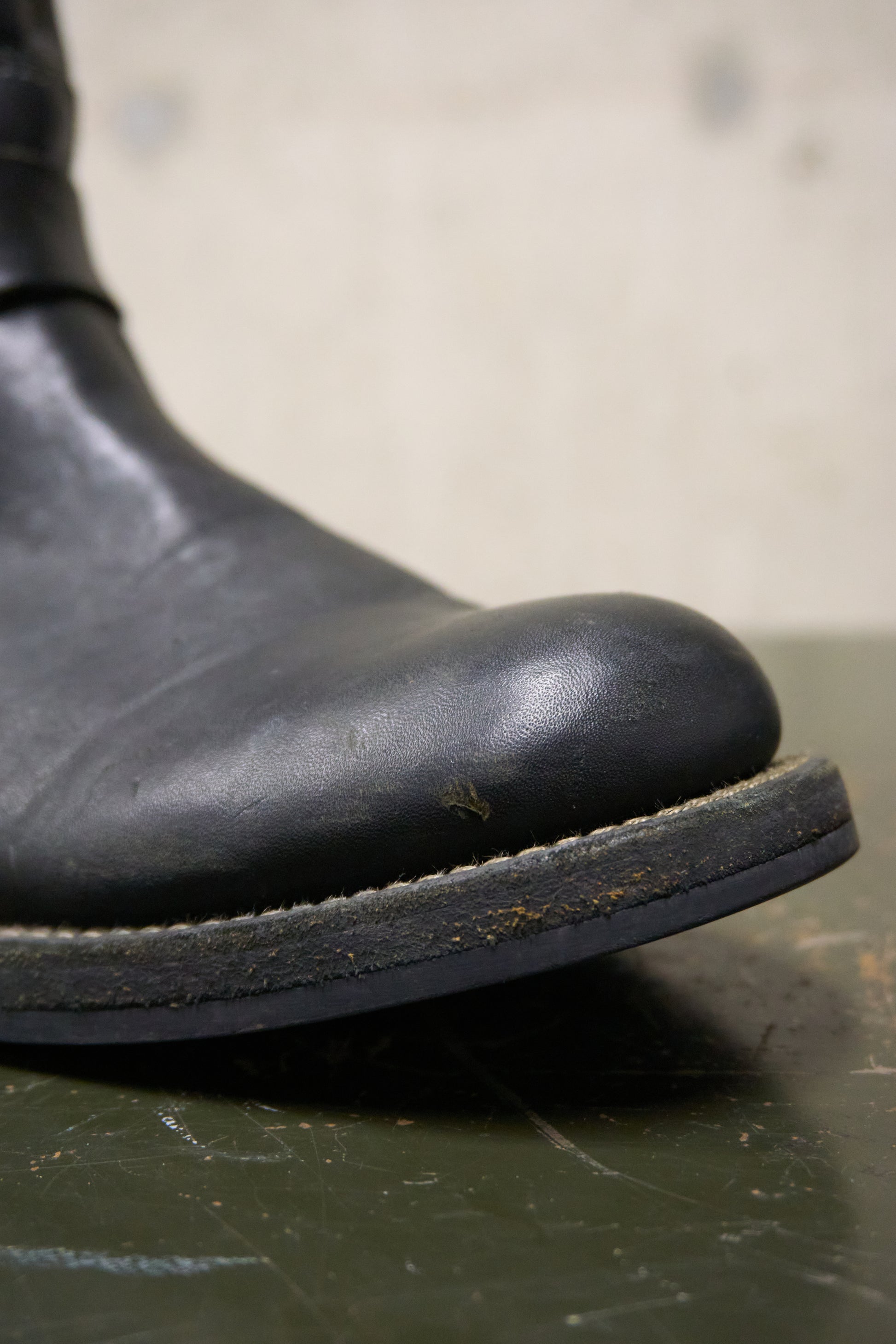 Close-up of a black leather boot sole on a textured surface with a blurred background