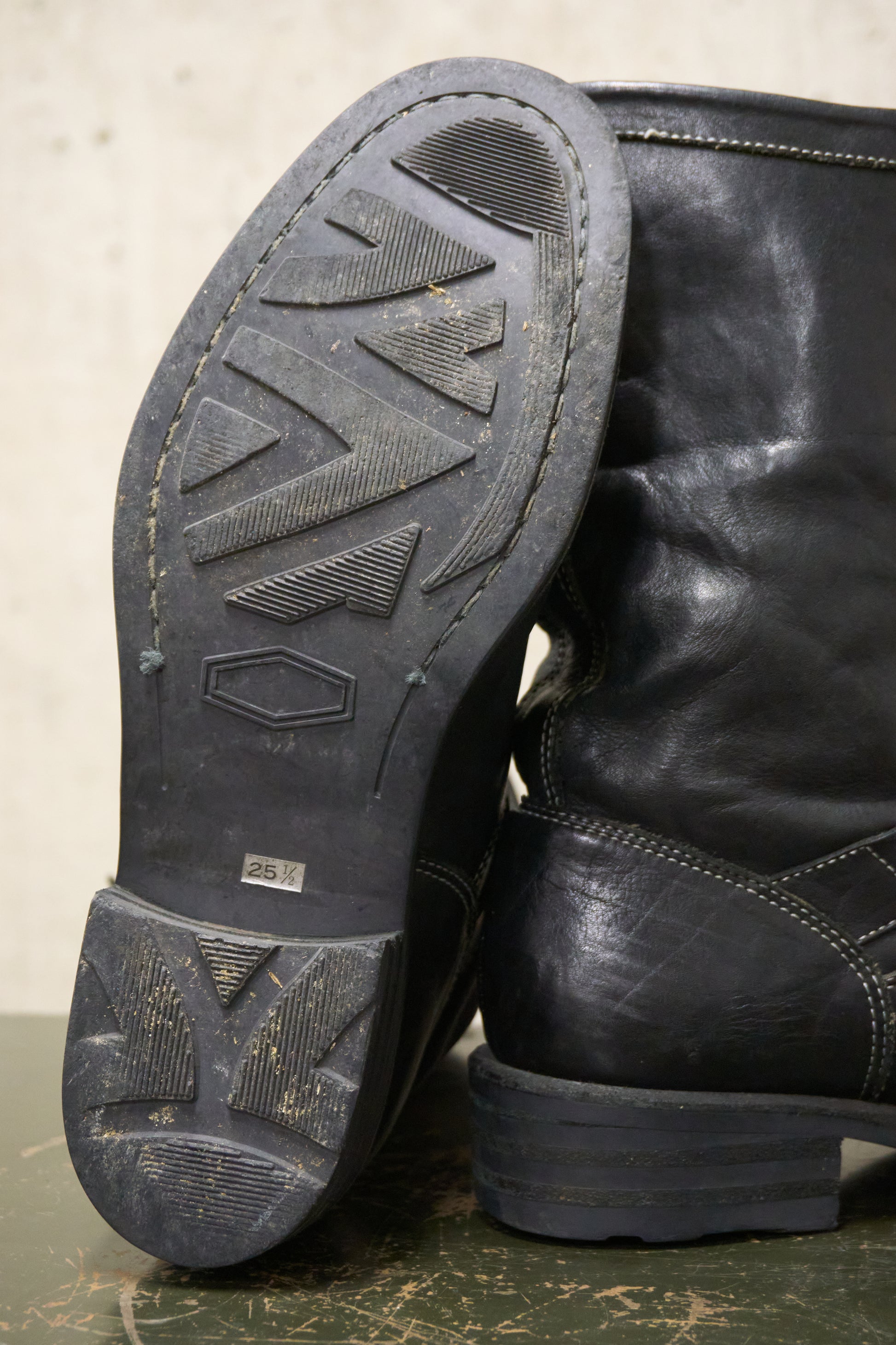 Close-up of black leather boots with a worn sole on a textured surface.