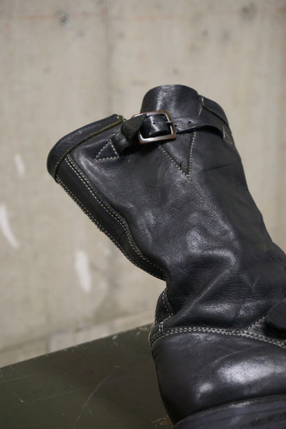 Black leather boot with a buckle on a concrete floor.