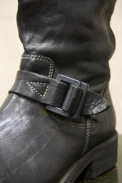 Close-up of a black leather boot with a buckle on a neutral background