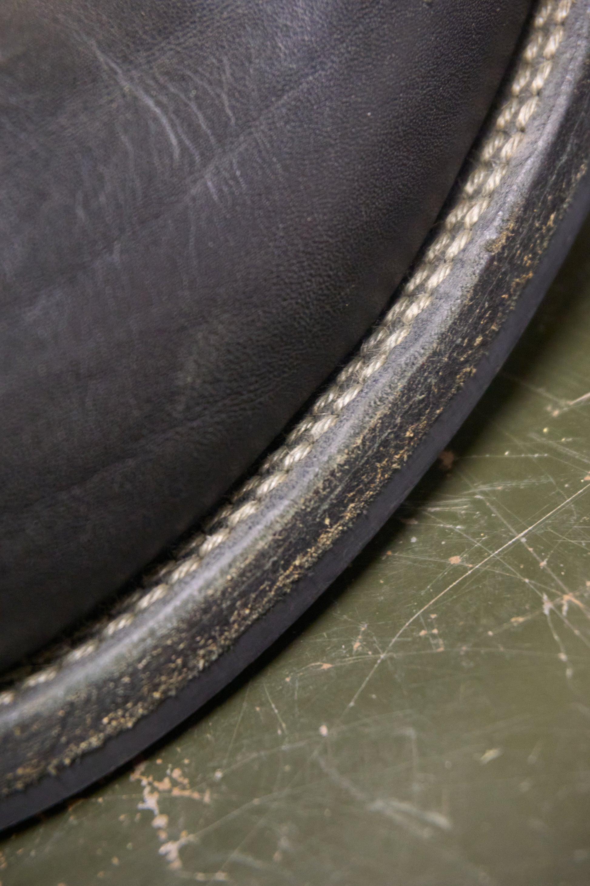 Close-up of a leather product with visible stitching on a green surface