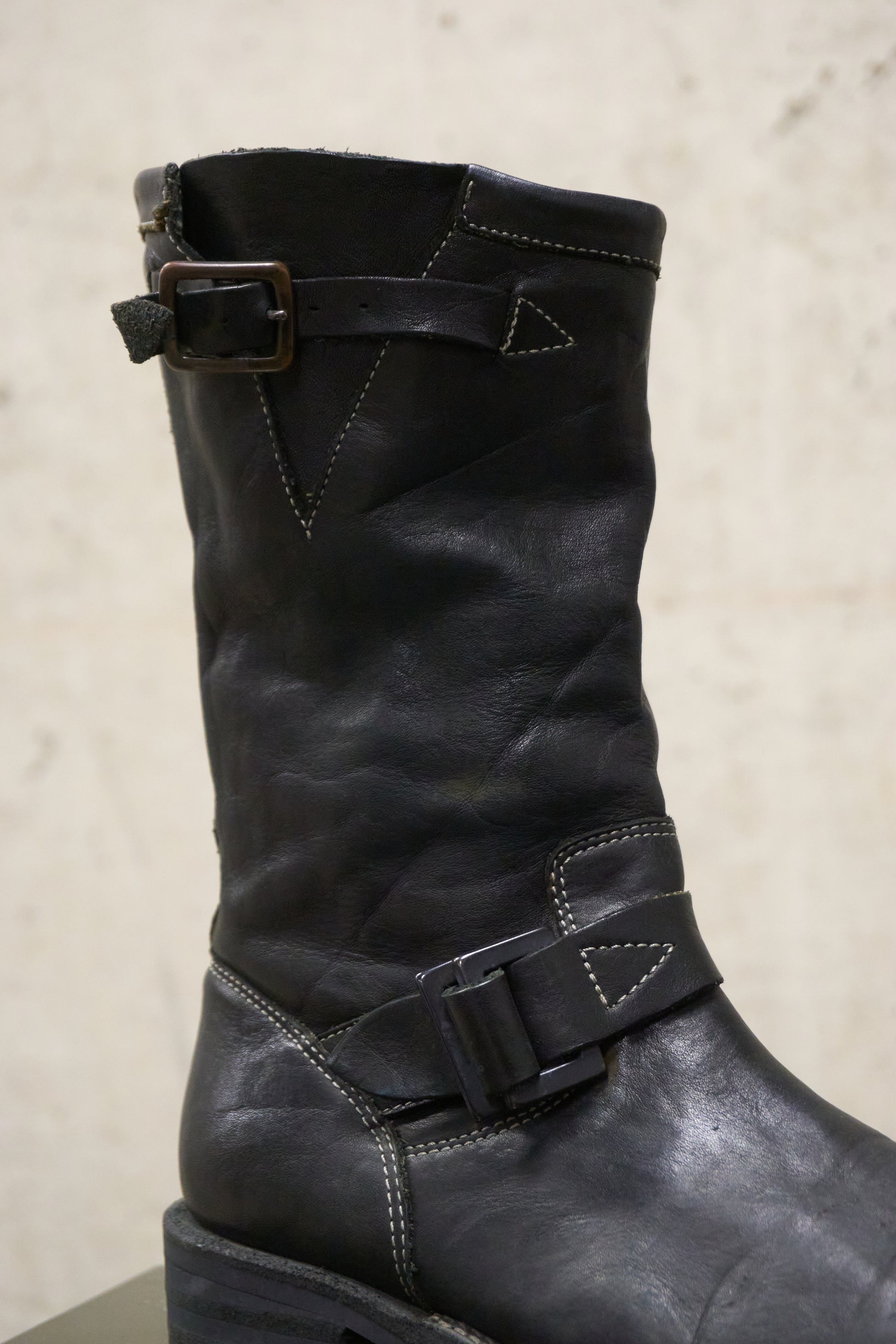 Black leather boot with buckles on a beige background