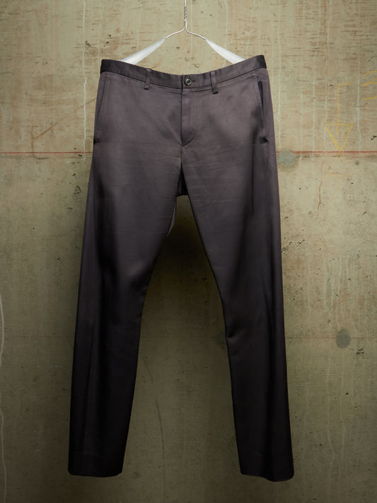 A pair of dark charcoal gray dress pants hanging from a white hanger against a textured concrete wall.