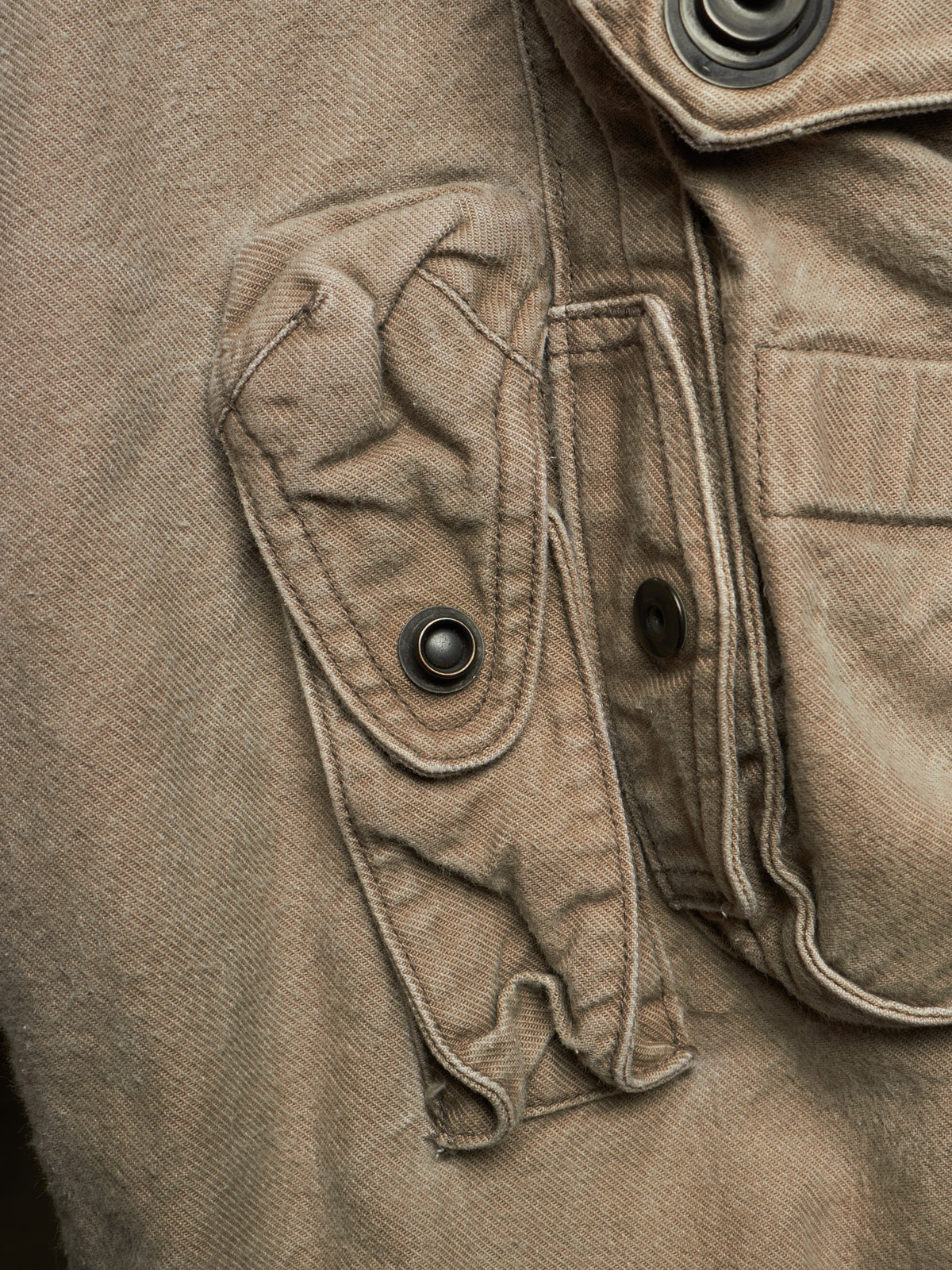 Close-up detail of a brown canvas utility jacket showing a buttoned flap pocket and metal snap buttons.