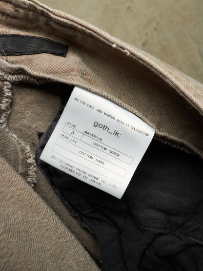 Close-up of the inside collar of a beige/tan garment showing a white sewn-in size and material label that reads 'goth_ik,' with dark inner lining visible.