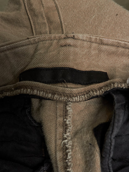 Close-up of a beige canvas jacket or vest showing the interior collar, raw hem stitching, and a black fabric label.