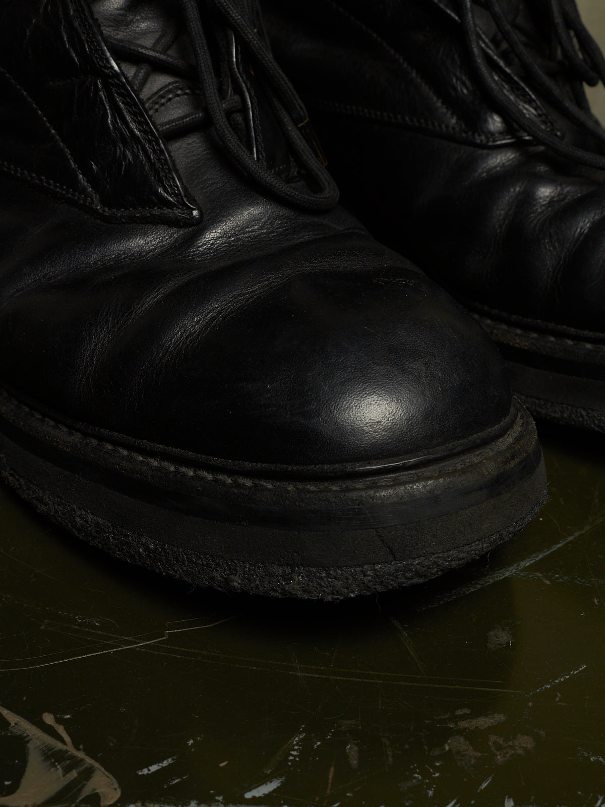 A close-up shot of a pair of black leather lace-up boots resting on a dark, reflective surface.