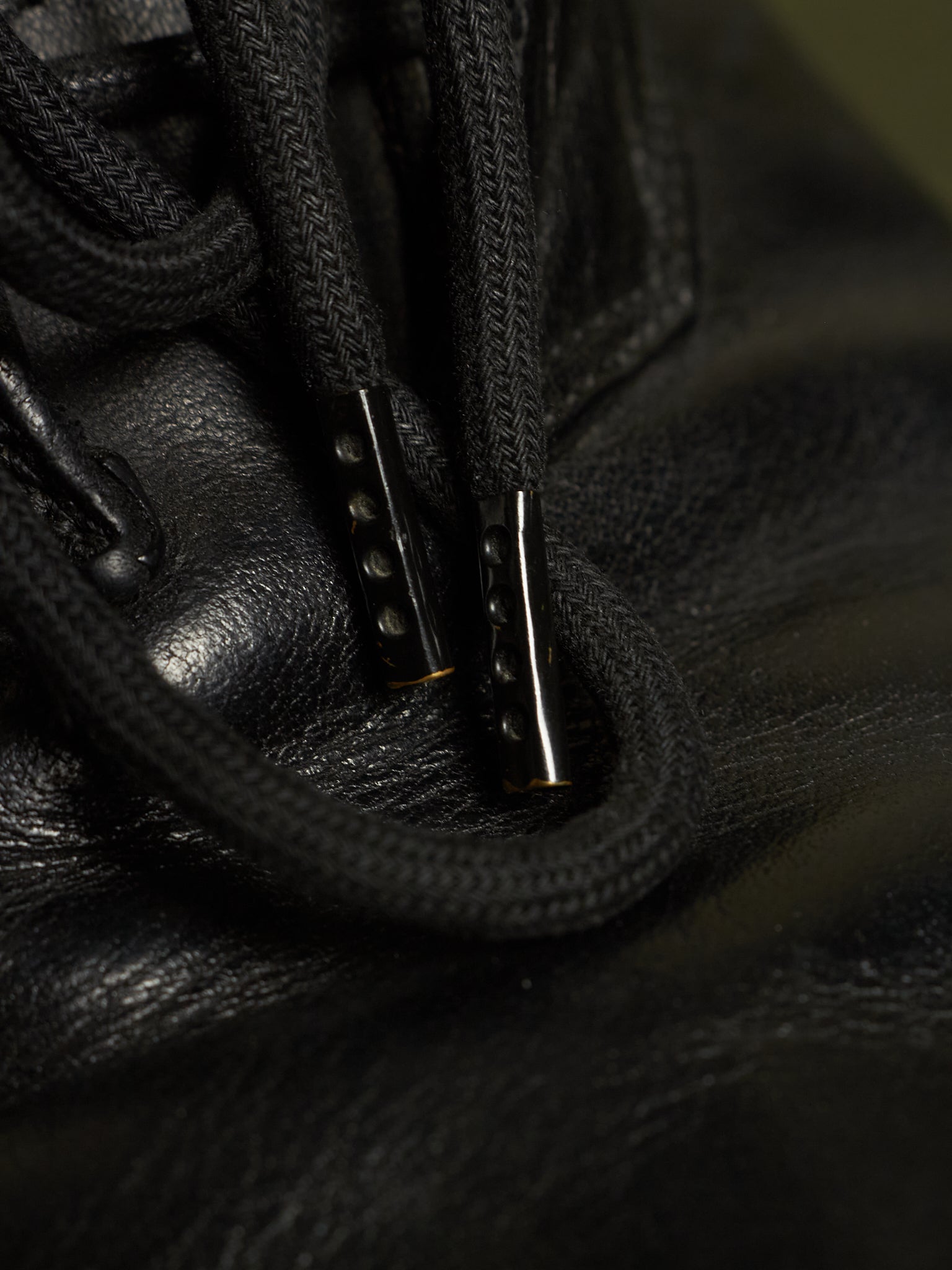 Close-up of black leather laces threaded through black metal eyelets on a black leather shoe or boot.