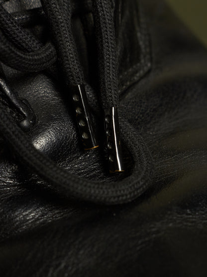 Close-up of black leather laces threaded through black metal eyelets on a black leather shoe or boot.