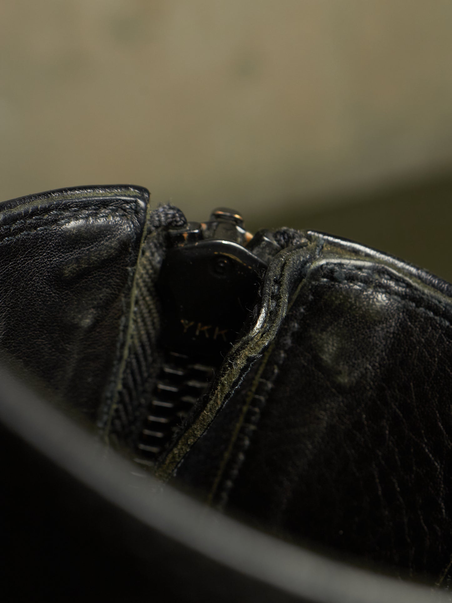 Close-up detail of a black leather zipper boot showing the textured leather, stitching, and a partially visible YKK zipper pull.