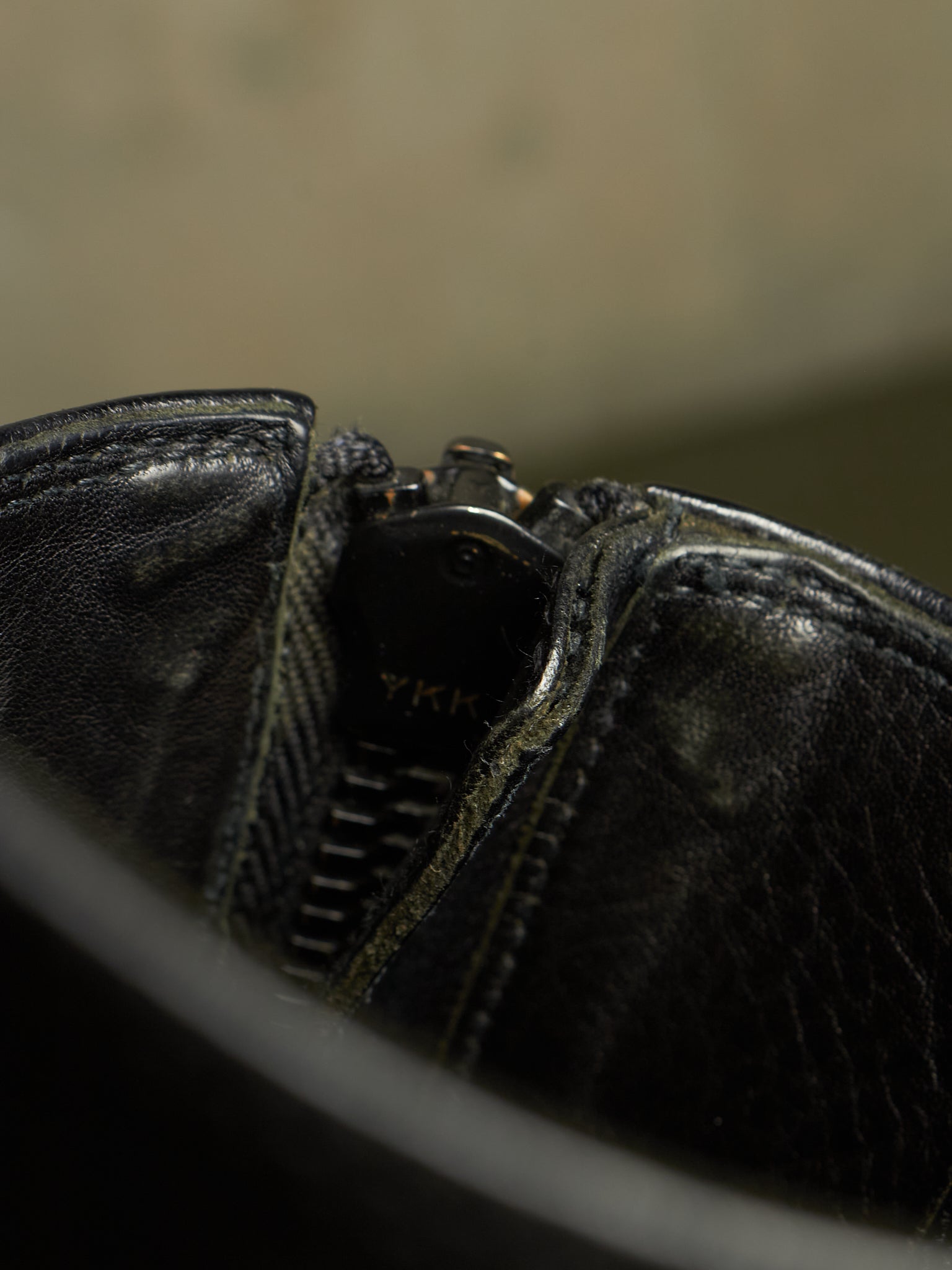 Close-up detail of a black leather zipper boot showing the textured leather, stitching, and a partially visible YKK zipper pull.