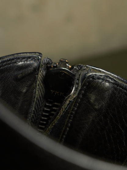 Close-up detail of a black leather zipper boot showing the textured leather, stitching, and a partially visible YKK zipper pull.