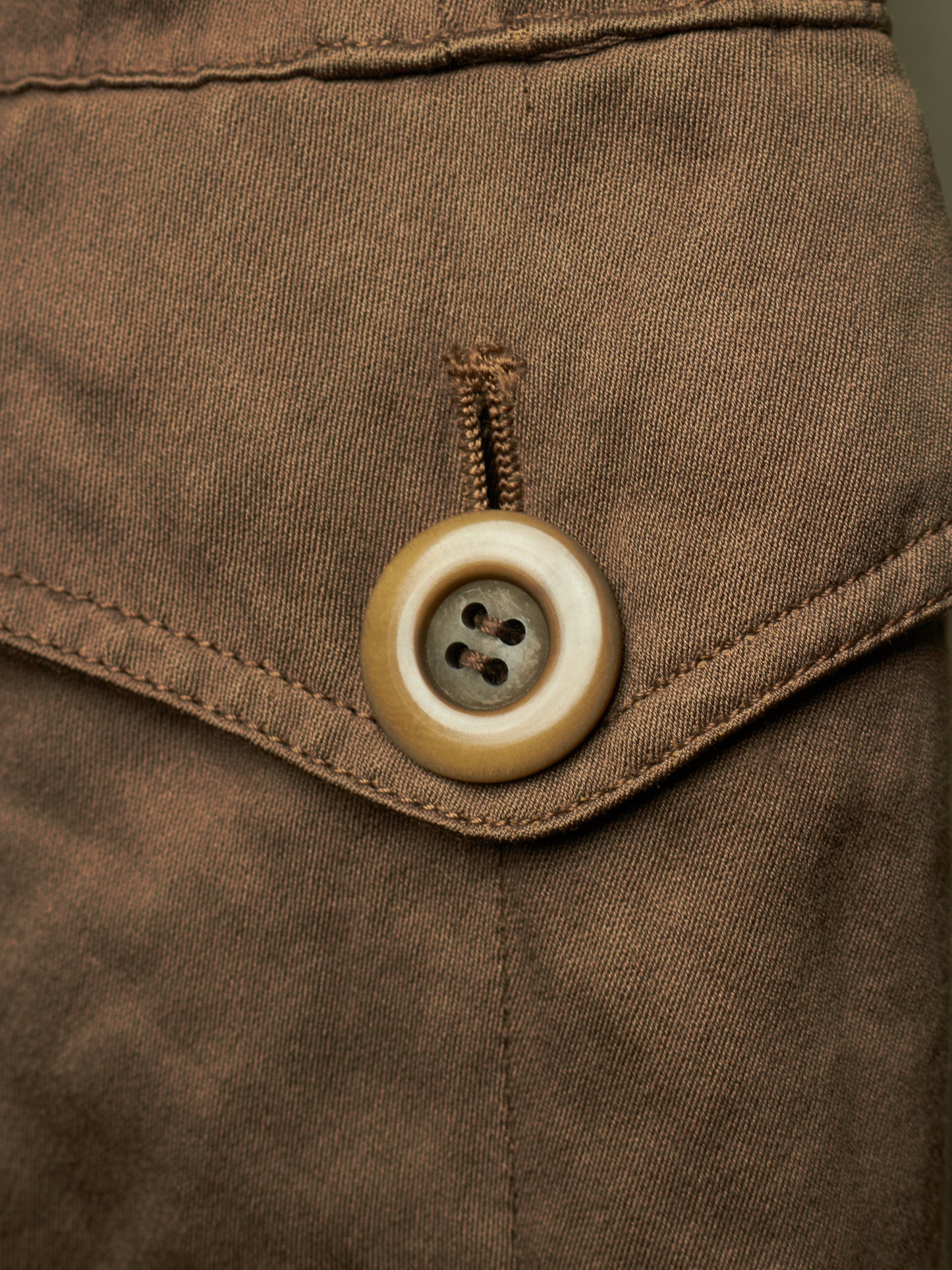 Close-up detail of a brown fabric garment featuring a brown buttoned flap pocket.