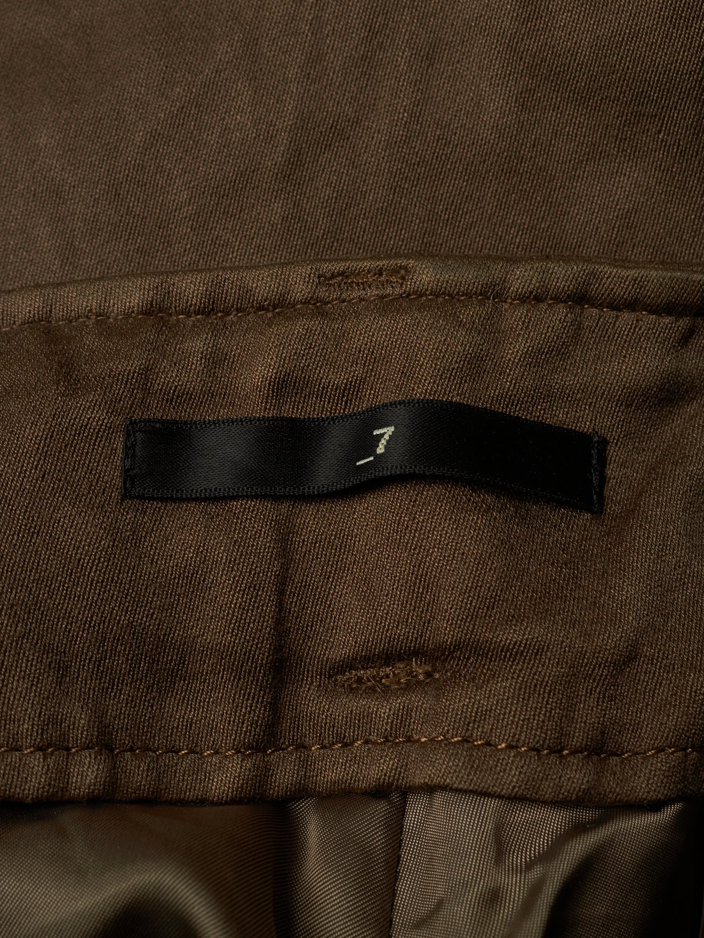 Close-up of a brown fabric garment showing a black fabric label with a small white stylized logo.